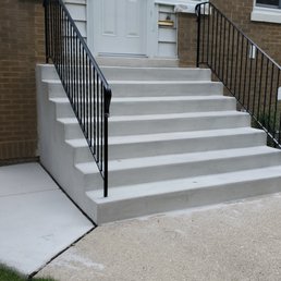 New stairs, side area, and tuckpointing on brick! - Concrete stairs with black metal railings lead up to a residential door, with a concrete ramp on the side for accessibility.