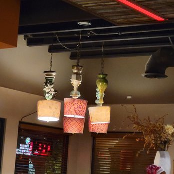 Range Cafe - My hubs noticed these before me. Gotta love it! - Four hanging lamps with colorful, patterned fabric shades are suspended from a dark ceiling with chains. The shades feature various designs, including floral and geometric patterns. The background includes a window with blinds, some decor, and a partial view of a person’s head at the bottom of the image. The setting appears to be a restaurant or cafe interior. - Breakfast & Brunch Near Me - Albuquerque, New Mexico