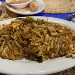 Pad Thai - A serving of Pad Thai with bean sprouts, chicken, and green onions on a white oval plate, garnished with a lime wedge.