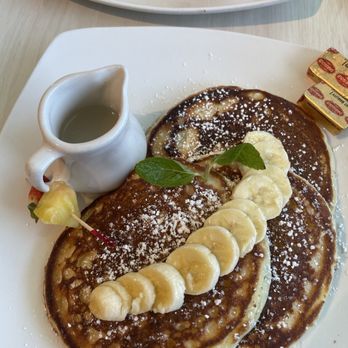 Puakea Grill - With a banana pancakes, covered in sliced bananas and powdered sugar with the side of coconut syrup. Two pats of butter if you need it. - American Near Me - Lihue, Hawaii