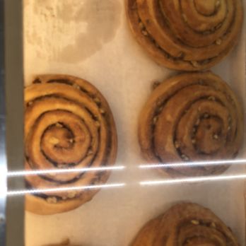 Shipley Do-Nuts - Four cinnamon rolls with swirled shapes are shown inside a display case, likely at a bakery or donut shop. - Donuts Near Me - Carrollton, Texas