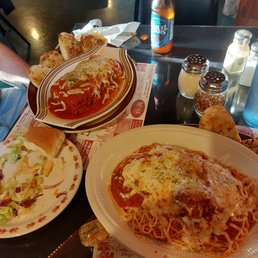 Meatballs - Spaghetti with melted cheese, a side salad with lettuce and radishes, and garlic bread are arranged on a restaurant table with condiments and a beer.