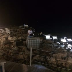 Shuluq - The DJ spins music while standing on the rocks of the beach.