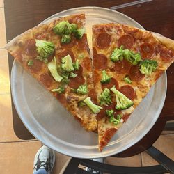 Two slices of pizza with pepperoni and broccoli.