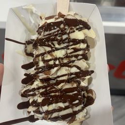 coconut bar dipped in white chocolate, topped with almonds and coconut, drizzled with dark chocolate.