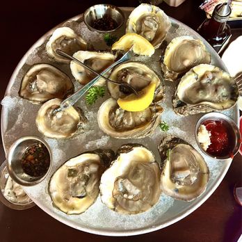Pappadeaux Seafood Kitchen - Chef Selection Oysters* - A large round tray filled with fresh oysters on ice, garnished with lemon wedges, parsley, and accompanied by dipping sauces. - Seafood Near Me - Albuquerque, New Mexico
