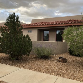 AMG Landscape - the front of a home in arizona - A residential house features desert landscaping with a pine tree, bushes, and rocks, under a cloudy sky, with a sidewalk in the foreground. - Irrigation Near Me