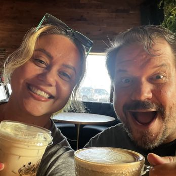 The Coffee Builders - Happy Friday! Best way to start a day, with amazing coffee :) - A woman and a man are smiling and holding coffee beverages inside a coffee shop with wooden interior and natural light. - Coffee & Tea Near Me - Phoenix, Arizona