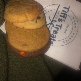 Snickerdoodle, chocolate chip, pumpkin and chocolate - these had a weird aftertaste- too much salt and butter - Three cookies, including snickerdoodle, chocolate chip, and pumpkin, are stacked on a Tiff's Treats paper bag, with some having a salty aftertaste.