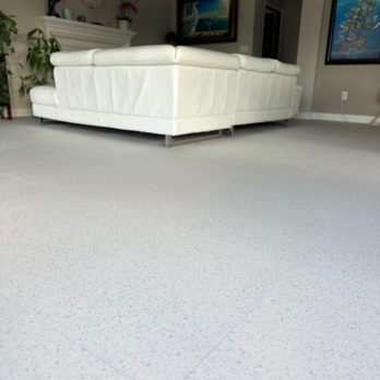 Divinity Flooring Services - A white sectional sofa is placed in a living room with framed artwork on the walls and potted plants, with a light-colored tiled floor. - Flooring Near Me