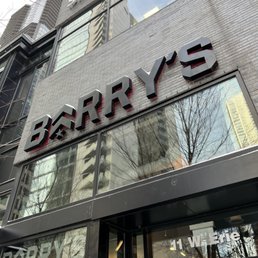 Entrance to Barry's River North. - The image shows the storefront of Barry's River North, a fitness studio in Chicago, with large black 3D signage and glass windows reflecting nearby buildings and trees.