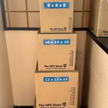 The UPS Store - Five cardboard boxes labeled with sizes from 6x6x6 to 14x14x14 are stacked against a wall in a retail or shipping store. - Shipping Centers Near Me - Arcadia, California