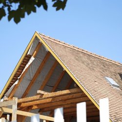Alliance Roof and Fence - Roof construction view showing exposed wooden framing beneath a partially opened gable, adjacent tile roofing, chimney, skyli...