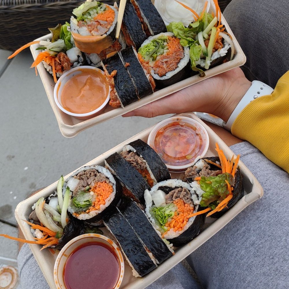 a person holding chopsticks over a tray of food a person holding chopsticks over a tray of food