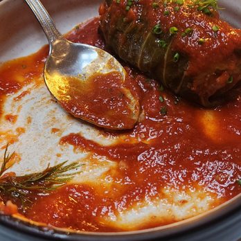 Sudova * Eastern European Kitchen - A close-up of a stuffed cabbage roll covered in tomato sauce, garnished with herbs, in a bowl at a restaurant. - Modern European Near Me - Cincinnati, Ohio