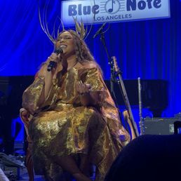 View of Lizzo sitting down from one of the front/center tables, next to the aisle not the stage