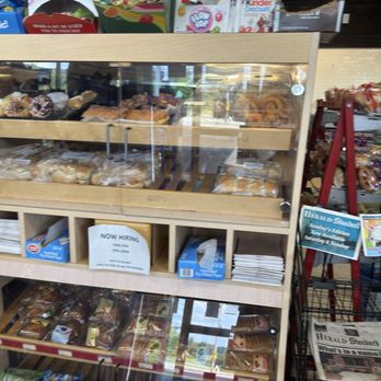 Sunoco A Plus Mini Mart - A wooden display case with glass panels contains assorted baked goods such as donuts, pastries, and bread, arranged on multiple shelves. The case is situated inside a store, with snack items and newspapers visible on nearby shelves and racks. The store appears to sell convenience items and baked goods. - Gas Stations Near Me - Pittsburgh, Pennsylvania