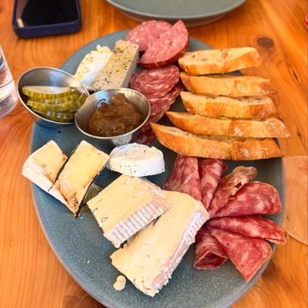 Sable Kitchen + Bar - A large charcuterie platter features cheeses, cured meats, pickles, and condiments on a wooden table, with empty plates and a phone nearby. - Salad Near Me - Lawrence, Kansas