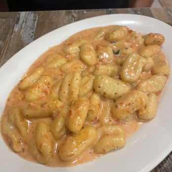 Che Tito's - Gnocchi - A white oval plate holds gnocchi covered in a creamy, orange-colored sauce, placed on a wooden table. - Pizza Near Me - Miami, Florida