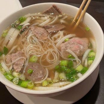 Pho 98 - A bowl of Vietnamese pho featuring rice noodles, slices of beef, and chopped green onions in broth, with chopsticks resting on the bowl. - Vietnamese Near Me - Chantilly, Virginia