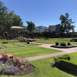 Beautiful heritage garden and architecture. - A well-maintained garden features a gazebo, brick pathways, flower beds, and trimmed bushes, with residential houses in the background.