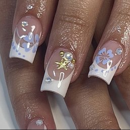 what i asked for - A set of acrylic nails features white French tips with blue floral and dot designs, adorned with pearls and gold embellishments.