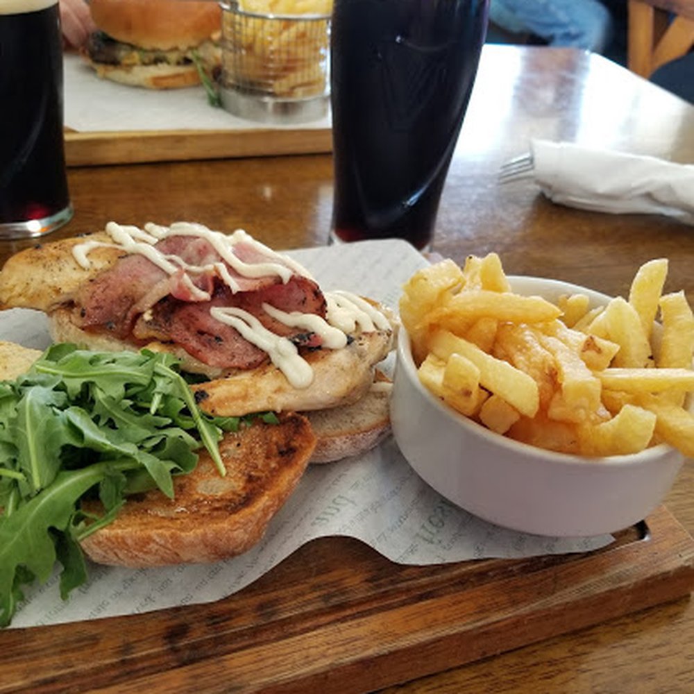 The Nook - Sliced chicken & crispy bacon with arugala on a chibatta bun with chips. Back ground is The Nook Steak Burger with chips, plus Guinness. - Cafes Near Me - Bushmills, MYL The Nook - Sliced chicken & crispy bacon with arugala on a chibatta bun with chips. Back ground is The Nook Steak Burger with chips, plus Guinness. - Cafes Near Me - Bushmills, MYL