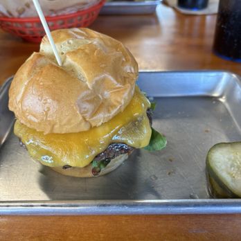 50 Burger - The 50 with cheddar! - A cheeseburger with cheddar cheese, lettuce, and a beef patty on a bun, served on a metal tray with pickles on the side. - Burgers Near Me - Salida, Colorado