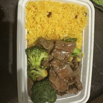Gold Dumpling - Beef with broccoli - A plastic takeout container holds yellow rice, broccoli, and beef with vegetables, served as a meal, on a dark surface. - Chinese Near Me - Groton, Connecticut