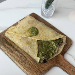 Savory Boulder Crepe - A crepe filled with ingredients and topped with green sauce, served on a wooden board in a modern café setting.