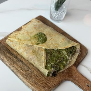Crepe Therapy Cafe - Boulder crepe (savory) - A crepe filled with ingredients and topped with green sauce, served on a wooden board in a modern café setting. - Creperies Near Me - Boulder, Colorado