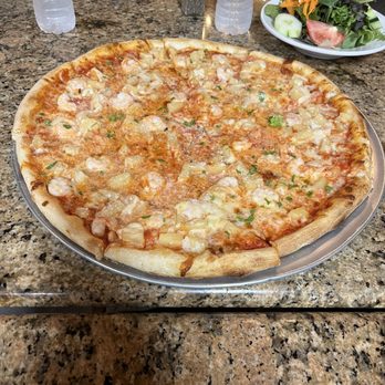 Avellino's Restaurant & Catering - Pizza - A cheese pizza topped with pineapple and ham slices is placed on a granite table, with bottled water and a salad in the background. - Italian Near Me - Medford, Massachusetts