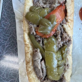 Bob-O's Hot Dogs - A hot dog in a bun is topped with green peppers, sliced beef, and a whole carrot, served on wax paper. The bun is soft and the toppings are arranged along the length of the hot dog. The image shows a close-up view of the hot dog with the toppings clearly visible. - Hot Dogs Near Me - Chicago, Illinois