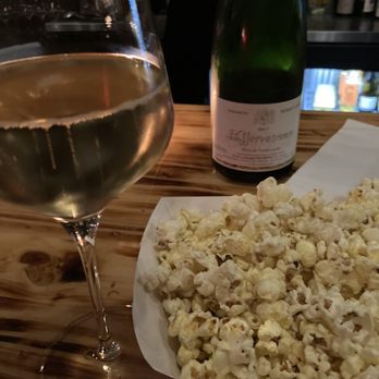 Post Off - A glass of white wine, a bottle of sparkling wine, and a bowl of popcorn are placed on a wooden table in a dimly lit setting. - Wine Bars Near Me - Grand Rapids, Michigan