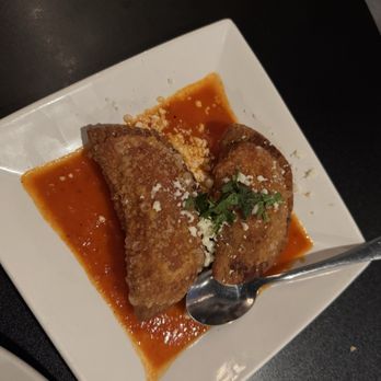 BoMallies - Mexican corn empanadas - Two Mexican-style empanadas are presented on a white square plate, topped with chopped herbs and cheese, with sauce underneath. - New American Near Me - Sheboygan, Wisconsin
