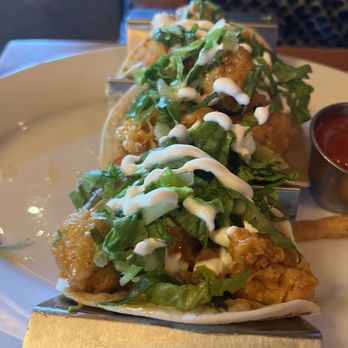 FD's Grillhouse - Fish tacos - Two fish tacos with fried fish, lettuce, and drizzled sauce are served on a plate with a side of ketchup. - American Near Me - Springfield, Missouri