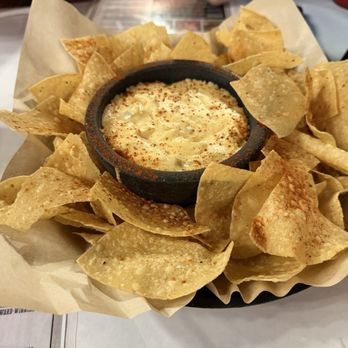 High Point Grill - Chips n Queso - Chips and queso served with a small cast iron skillet of melted cheese dip, surrounded by tortilla chips, on a restaurant table. - Sandwiches Near Me - Albuquerque, New Mexico