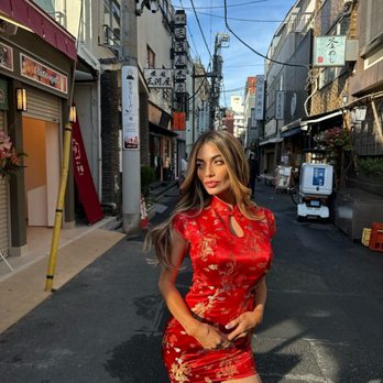 Kim's Alterations - A woman wearing a red, gold-embroidered dress poses on a narrow street lined with small shops and signs in Japanese. - Sewing & Alterations Near Me - Albuquerque, New Mexico