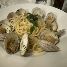 Linguine Alle Vongole - A serving of linguine alle vongole features cooked pasta with a handful of open clams arranged around the pasta, garnished with chopped parsley. The dish is presented on a white, round plate, with a simple and elegant presentation suitable for an Italian restaurant specializing in Northern Italian cuisine.