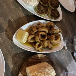 Calamari - Plate of fried calamari with lemon wedge, zucchini fritters with sour cream, and a piece of bread on a wooden table.