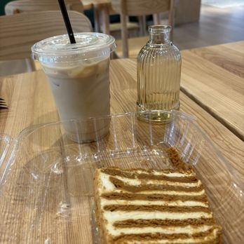 Cube Coffee - A natural-looking wooden table holds an iced coffee drink and a slice of honey cake, made of layers of brown sponge and cream filling. - Coffee & Tea Near Me - Ellicott City, Maryland Cube Coffee - A natural-looking wooden table holds an iced coffee drink and a slice of honey cake, made of layers of brown sponge and cream filling. - Coffee & Tea Near Me - Ellicott City, Maryland