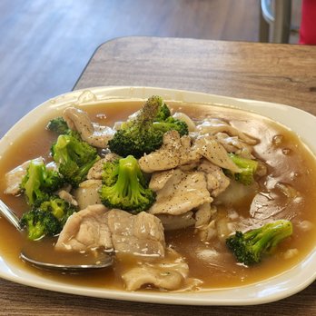 Thai Buri - Lad Nar - A dish featuring sliced chicken and broccoli florets in a brown sauce, served on a white oval plate at a restaurant. - Thai Near Me - Wheeling, Illinois