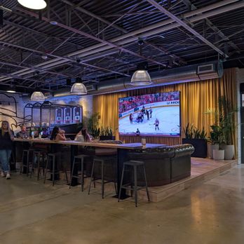 Pins Mechanical - Seating - A sports bar interior features a large TV displaying a hockey game, with seating including bar stools and a curved leather couch, and potted plants near the stage. - Bowling Near Me - Austin, Texas