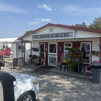 Burger Time - Elk River Burgers' exterior features a white building with red accents, outdoor seating, and decorative plants, under a blue sky. - Burgers Near Me - Pineville, Missouri