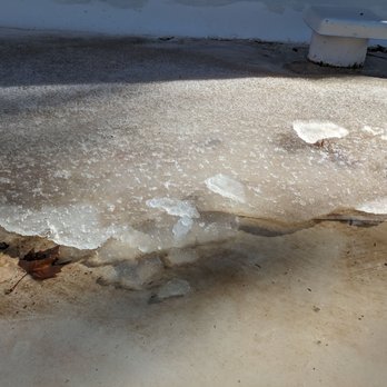 Paramount Roofing - The ice from melted snow is at least an inch thick - Melting ice and snow create a thin, uneven layer on the ground near a vent, with some leaves and dirt visible. - Roofing Near Me - Albuquerque, New Mexico