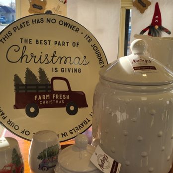 Sweet Things Chocolates - Canisters, cookie plates, assorted dishware. - The image shows a collection of white ceramic kitchenware, such as jars, pitchers, and small containers, arranged on a surface near a window. Behind the items, there is a round decorative sign with a Christmas message and a red truck illustration, emphasizing a holiday theme. The background includes a window with a parking lot and some outdoor scenery visible. - Candy Stores Near Me - Indianapolis, Indiana