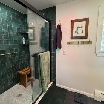 Denver Remodels - After decorating - A bathroom features a glass shower with green tiled walls, a wooden stool inside, and a towel hanging on the shower door. - General Contractors Near Me