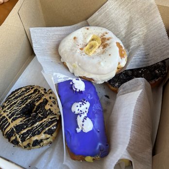 Voodoo Doughnut - Butterfinger (black with drizzle) - custard cream & banana - custard cream filled doughnut (purple haze) - Donuts Near Me - San Antonio, Texas