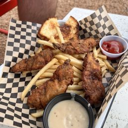 Country Fried Steak " Wings - A tray of fried chicken tenders with French fries, toast, and dipping sauces, served on checkered paper at an outdoor setting.