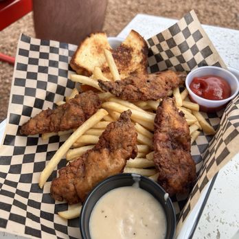 Chalmers - Country Fried Steak Tenders - A tray of fried chicken tenders with French fries, toast, and dipping sauces, served on checkered paper at an outdoor setting. - Bars Near Me - Austin, Texas